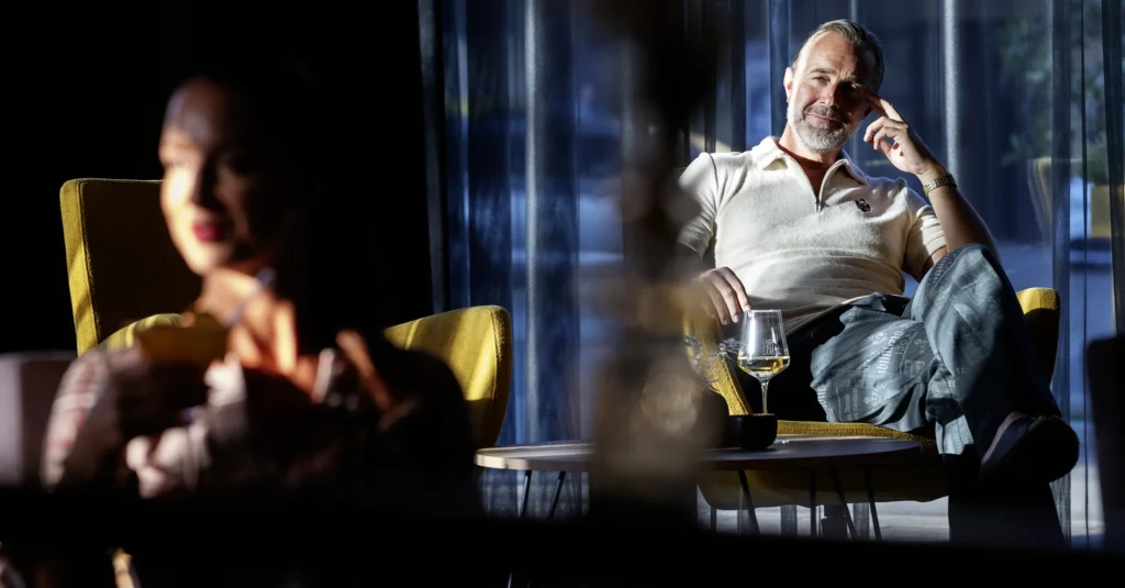 Cinematic Businessportrait eines stilvoll gekleideten Mannes in Lounge-Atmosphäre mit Weinglas und dramatischem Licht – fotografiert von Michael Preschl, Werbefotograf und Visual Brand Specialist aus Salzburg.