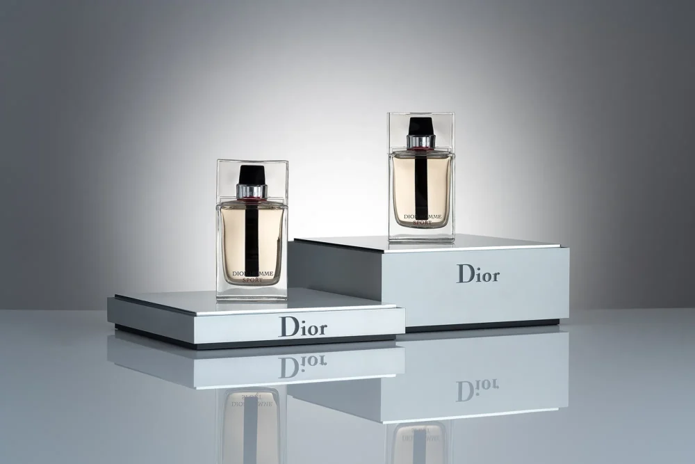 Sport. Precision. Dior Homme — Product Photography by Michael Preschl Zwei Flakons Dior Homme Sport Eau de Toilette auf gestuften silbernen Dior-Markendisplays mit Spiegeluntergrund vor grauem Hintergrund – Produktfotografie Brand Visual, Fotograf Michael Preschl