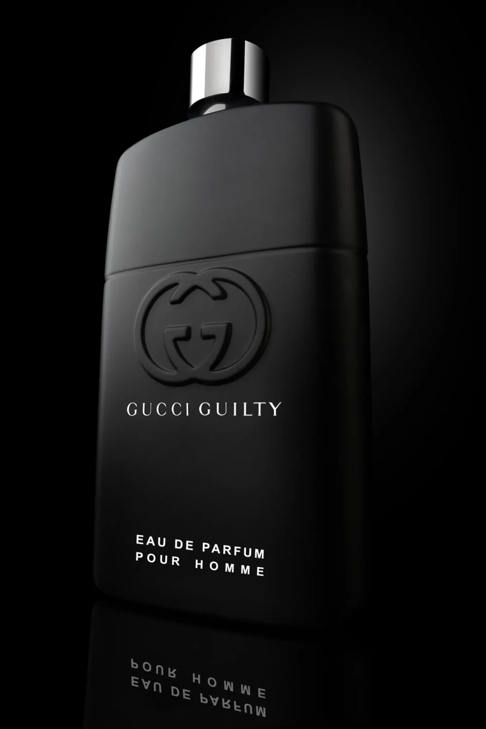 Guilty. Gucci — Product Photography by Michael Preschl Gucci Guilty Eau de Parfum Pour Homme in mattschwarzem Flacon mit geprägtem GG-Logo und silbernem Zerstäuber auf schwarzer Spiegelfläche vor dunklem Hintergrund – Produktfotografie Brand Visual, Fotograf Michael Preschl