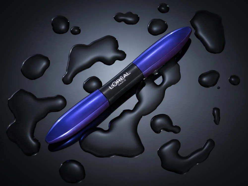 Ink. Intensity. L'Oréal Paris — Product Photography by Michael Preschl L'Oréal Paris Mascara in blau-violettem Gehäuse diagonal auf dunklem Untergrund mit schwarzen Tintenpfützen und Spritzern arrangiert – Produktfotografie Flatlay, Fotograf Michael Preschl